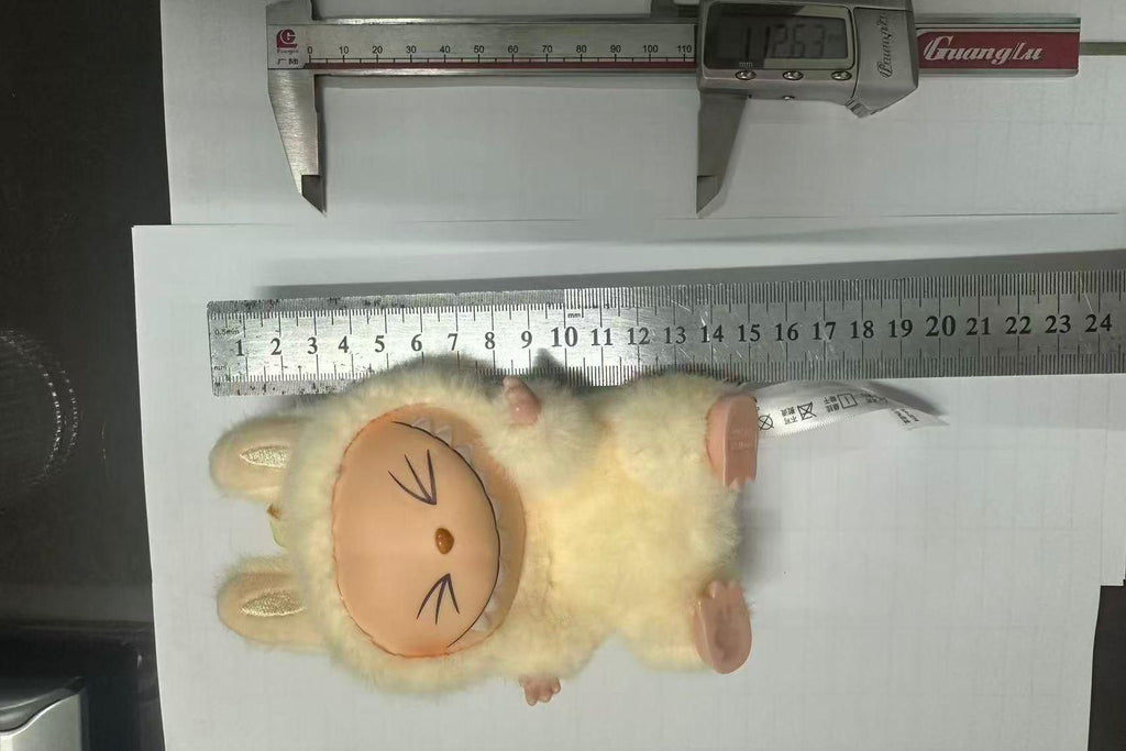 Small plush toy resembling a cat with measurement tools on a white background